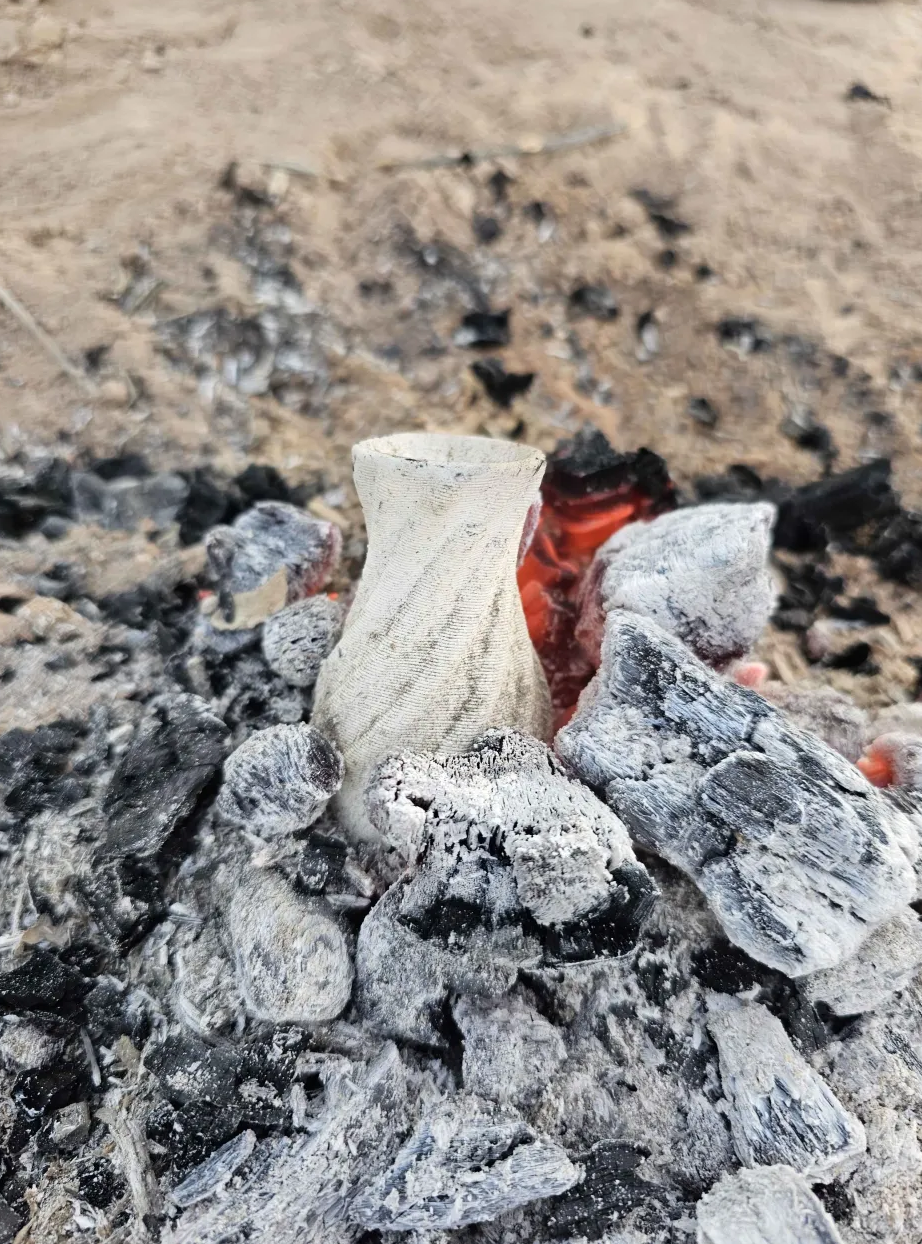 A ceramic vessel cooling in campfire coals